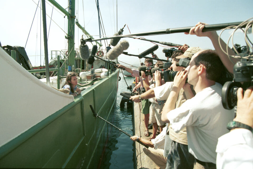 La militante est sur le bateau et les journalistes sur le quai. Les micros tendus au dessus de l'eau. - Stephanie Mills, campaigner à bord du RAINBOW WARRIOR, tient une conférence de presse à Tahiti en route pour Moruroa pour protester contre les essais nucléaire français. © Steve Morgan / Greenpeace
