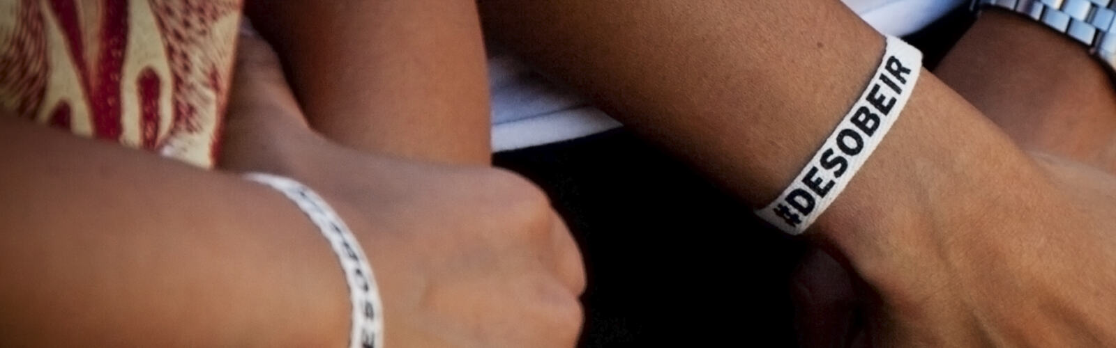 Des bras vêtus d'un bracelet portant la mention désobéir - Personnes portant des bracelets « Désobéir » pour la commémoration du 30e anniversaire de l'attenat du Rainbow Warrior. Les membres de Greenpeace et des activistes de la société civile se sont mobilisés ensemble sous la Tour Eiffel pour défendre notre droit à la désobéissance et honorer la mémoire et le courage de Fernando. © Tanya Ross / Greenpeace