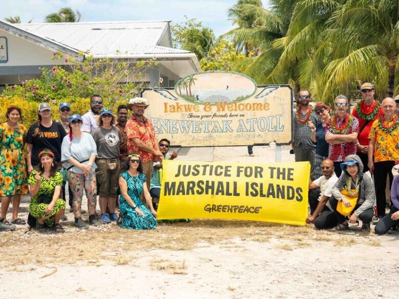 Greenpeace staff and Rainbow Warrior crew holding 'Justice for Marshall Islands' banner.