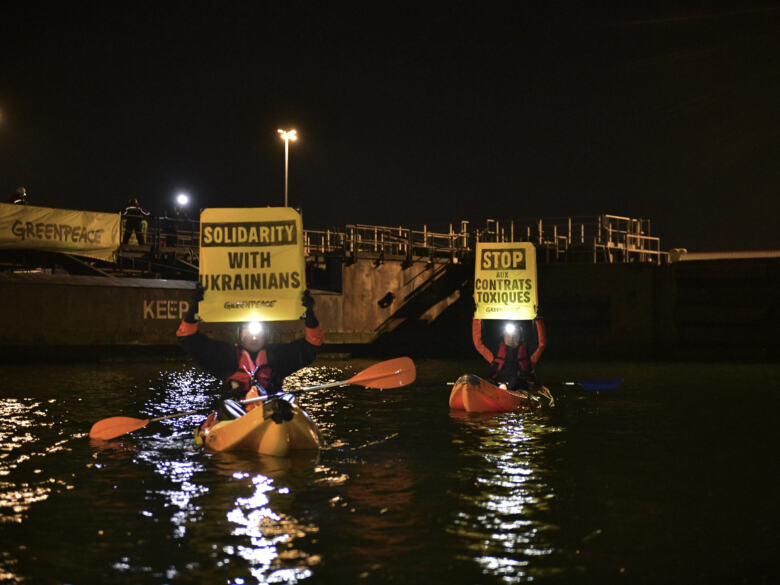 Deux activistes dans des kayaks portent chacun une banderole : Solidarity with ukrainians, et Stop aux contrats toxiques