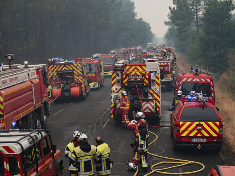 Des camions de pompiers et des pompiers s'alignent sur une route forestière pendant une importante intervention contre un incendie à Saint-Hélène en Gironde.