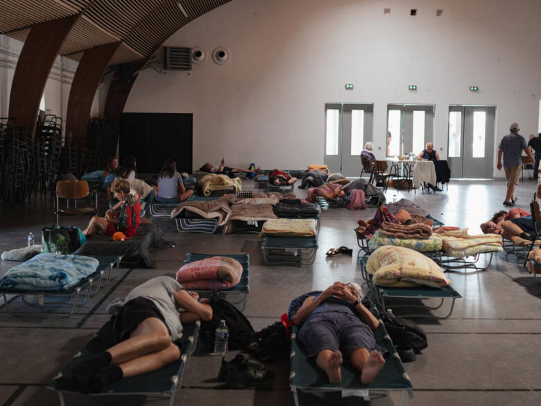 Des personnes se reposent sur des lits de camp dans une grande salle publique utilisée comme centre d'accueil d'urgence pendant une évacuation liée à un incendie au Porge en Gironde.